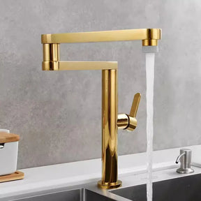 An Allfixture Deck Mounted Kitchen Faucet with Foldable Pot Filler is installed on a white counter. This modern faucet features a brushed gold finish, a single lever handle, and a tall, rectangular spout design with water flowing into the sink below. The background includes a light gray wall and part of another sink.