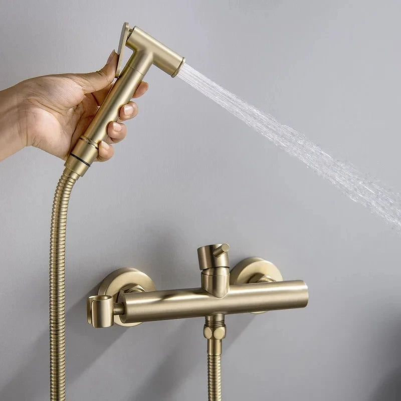 The Tiqui Cold And Hot Water Wall Mounted Bidet Faucet, featuring a sleek, gold-toned finish with a cylindrical control handle and flexible hose, boasts a minimalist yet contemporary design. This modern fixture, reminiscent of premium bathroom faucets, is mounted on a gray wall for an elegant look.