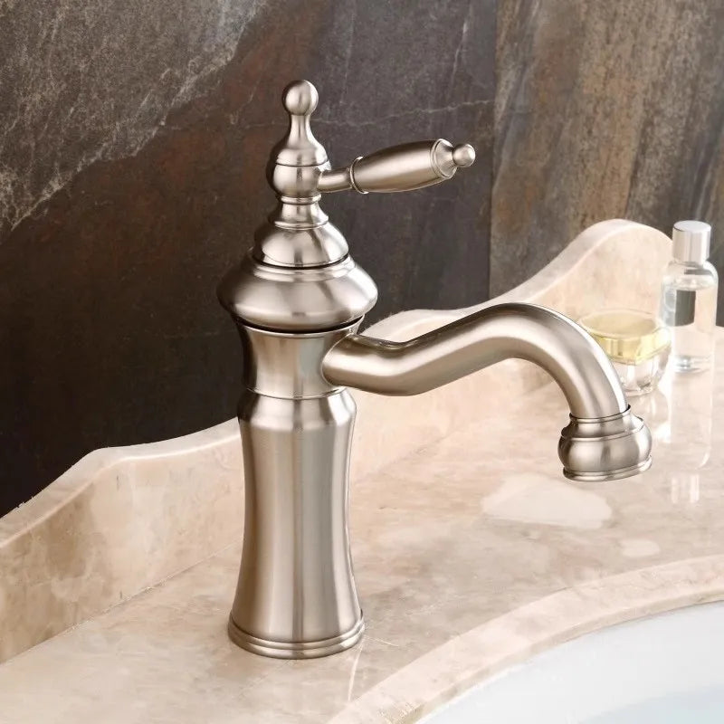 An Allfixture Solid Brass Single Handle Swivel Spout Bathroom Sink Faucet with a classic, vintage design is mounted on a marble countertop. The background features a stone wall, and a small bottle and container are seen next to the faucet.