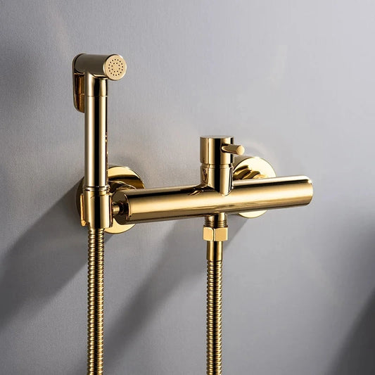 The Tiqui Cold And Hot Water Wall Mounted Bidet Faucet, featuring a sleek, gold-toned finish with a cylindrical control handle and flexible hose, boasts a minimalist yet contemporary design. This modern fixture, reminiscent of premium bathroom faucets, is mounted on a gray wall for an elegant look.