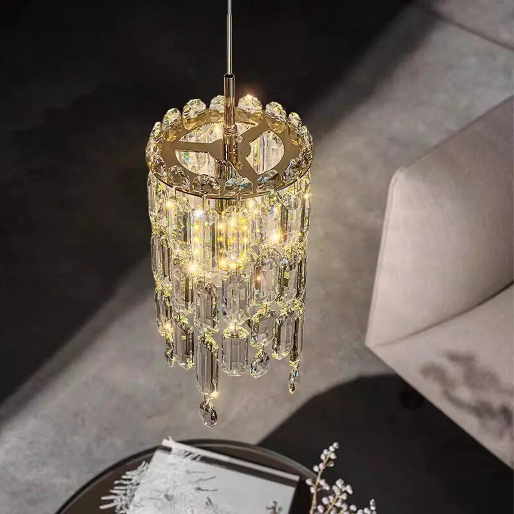 The Morsale Gio Crystal Pendant Light with cascading crystal-like pendants and LED bulbs emits a warm glow above a modern living space, partially illuminating a plush armchair and floral centerpiece, enhancing the room's sophisticated ambiance.