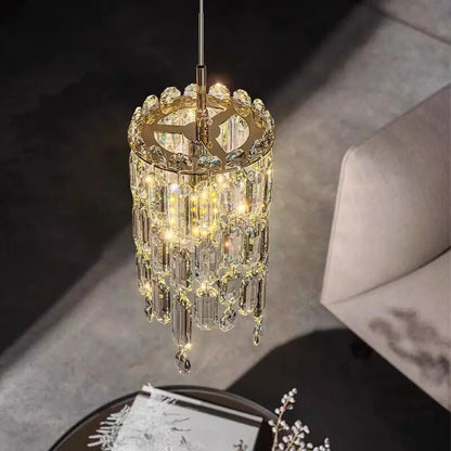 The Morsale Gio Crystal Pendant Light with cascading crystal-like pendants and LED bulbs emits a warm glow above a modern living space, partially illuminating a plush armchair and floral centerpiece, enhancing the room's sophisticated ambiance.