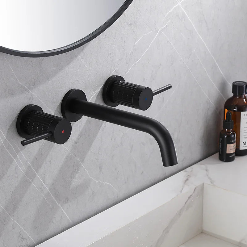 A modern bathroom sink features the Brushed Gold 8-Inch Bathroom Faucet by Allfixture, boasting a sleek wall-mounted design with two matching control handles that provide the perfect hot & cold mixer. The countertop is marble, and various toiletries, including bottles, are placed on the side. The wall is adorned with a large round mirror.