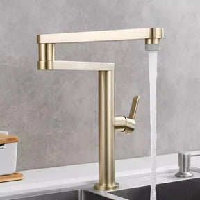 An Allfixture Deck Mounted Kitchen Faucet with Foldable Pot Filler is installed on a white counter. This modern faucet features a brushed gold finish, a single lever handle, and a tall, rectangular spout design with water flowing into the sink below. The background includes a light gray wall and part of another sink.