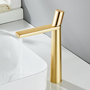 An AllFixture Solid Brass Single Handle Bathroom Basin Faucet with a modern gold finish and sleek, straight design is installed on a white countertop. The faucet is turned on, releasing a gentle stream of water into the white basin sink, creating small bubbles. The background features light gray and white decor.