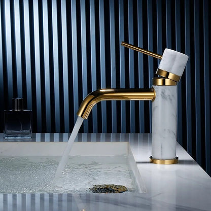 The Solid Brass & Marble Bathroom Faucet by allfixture enhances a modern bathroom sink with its sleek, gold finish and marble handle, placed beside a small square bottle of dark-colored liquid. The backdrop of vertically aligned blue and black slats perfectly complements the minimalist and sophisticated design of the bathroom faucet.