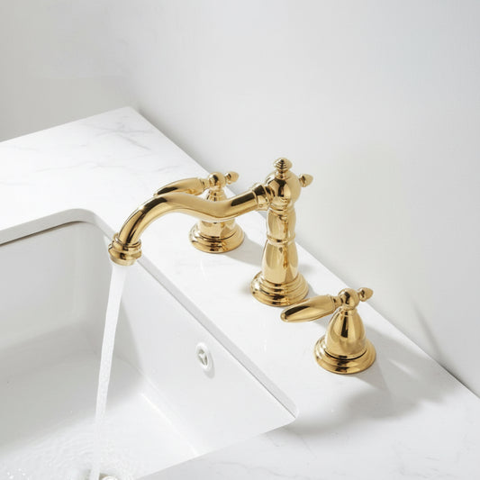 The Tiqui Maison Widespread Bathroom Faucet, featuring a gold finish and two handles, elevates a white marble sink countertop as water streams gracefully from its spout into the basin.