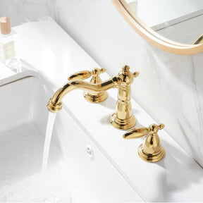 A Tiqui™ Solid Brass Contemporary Bathroom Sink Faucet, featuring a curved spout and two matching handles, is elegantly installed on a white marble countertop with a gray marble backsplash. Water flows from the faucet into the white sink below. A blue towel is partially visible on the left side.