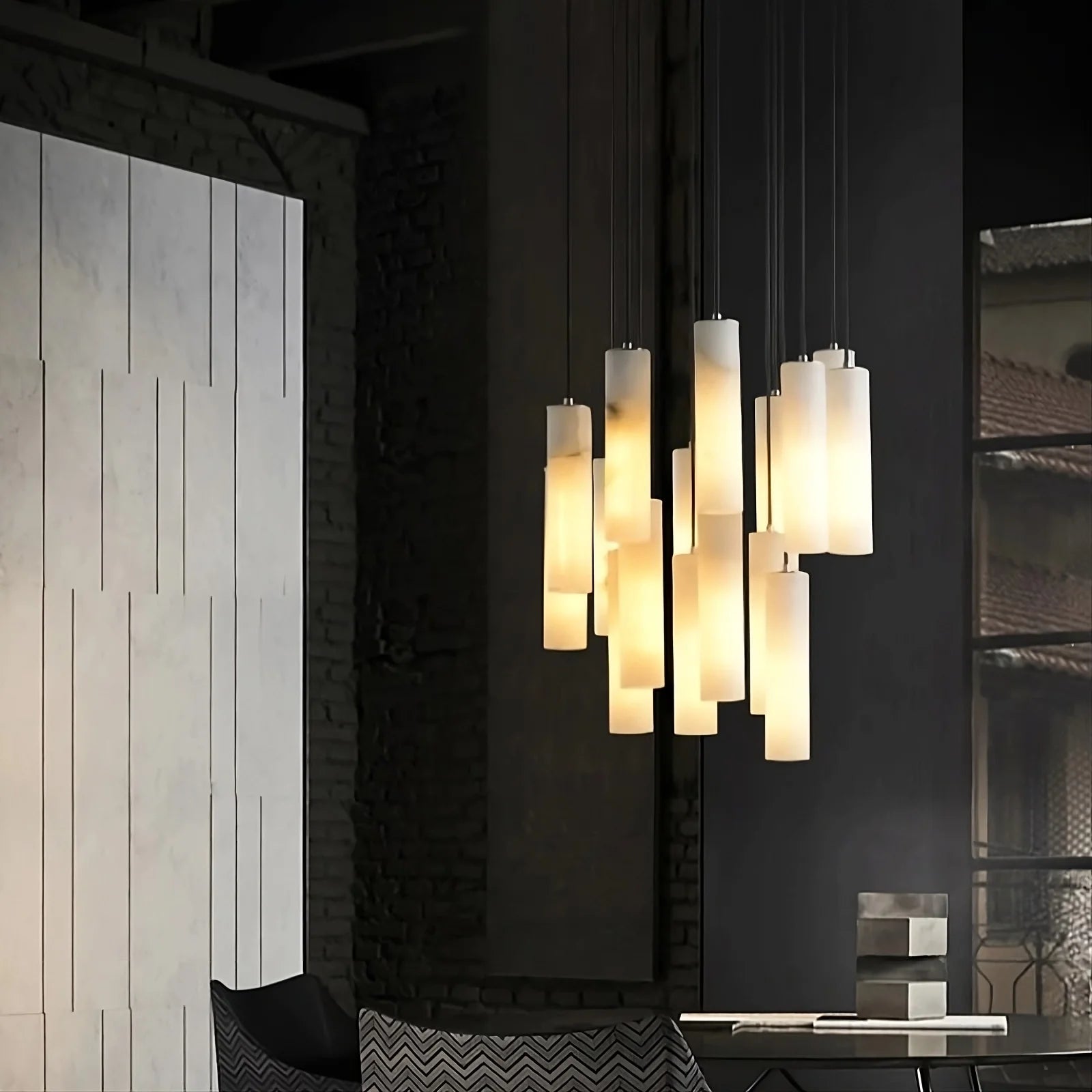 A modern interior showcases a cluster of Morsale.com's Moonshade™ Marble Pendant Lighting Fixtures, each one emitting a warm glow from dimmable LED bulbs. The space features a textured wall on the left and a dark, dimly lit area with a window and various decor elements on the right. The overall ambiance is cozy and contemporary.