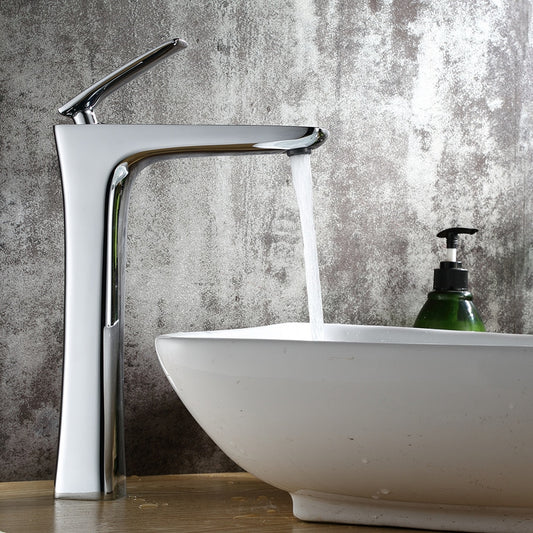 The Wasser™ Chrome Bathroom Faucet by Wanfan features water flowing into a white, bowl-shaped sink set on a wooden countertop. A green soap dispenser is placed beside the sink, complementing the textured grey wall in the background.