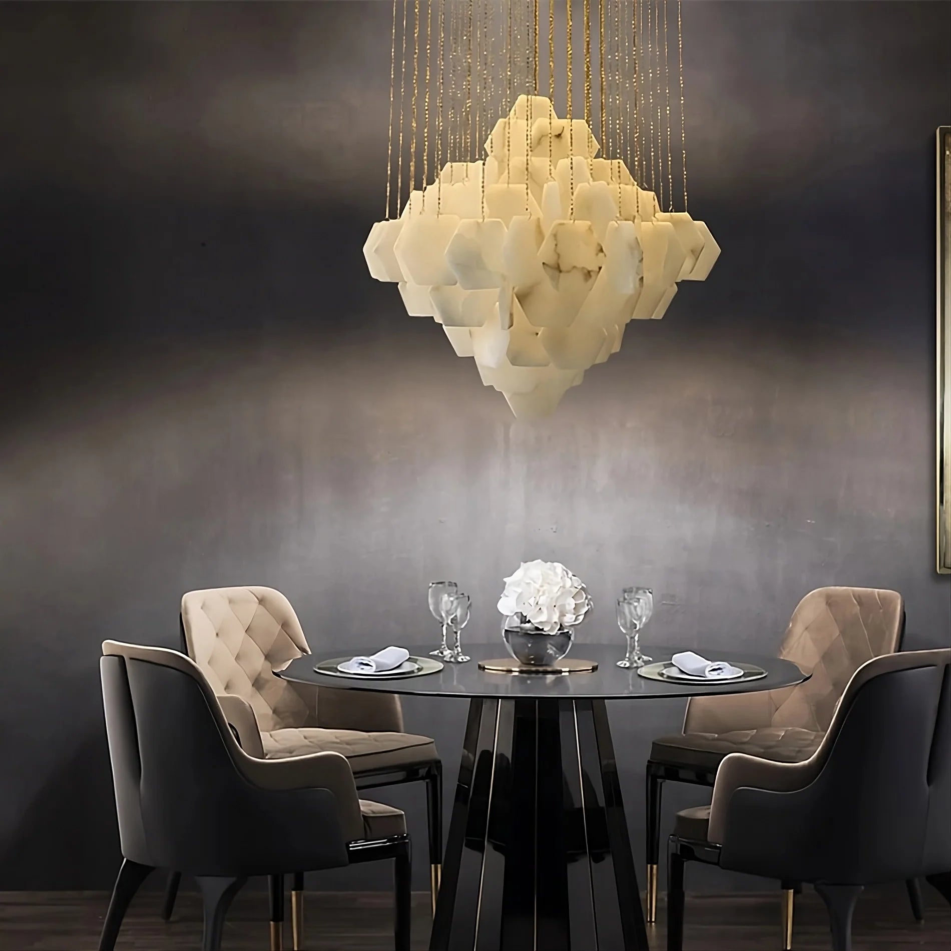 A modern dining area featuring a round glass-top table with a black base, surrounded by four upholstered chairs in beige and black. Above the table hangs the **Moonshade Natural Marble Modern Chandelier** by **Morsale.com**, with geometric, translucent, white cloud-like shapes. The ambiance is sophisticated and elegant.