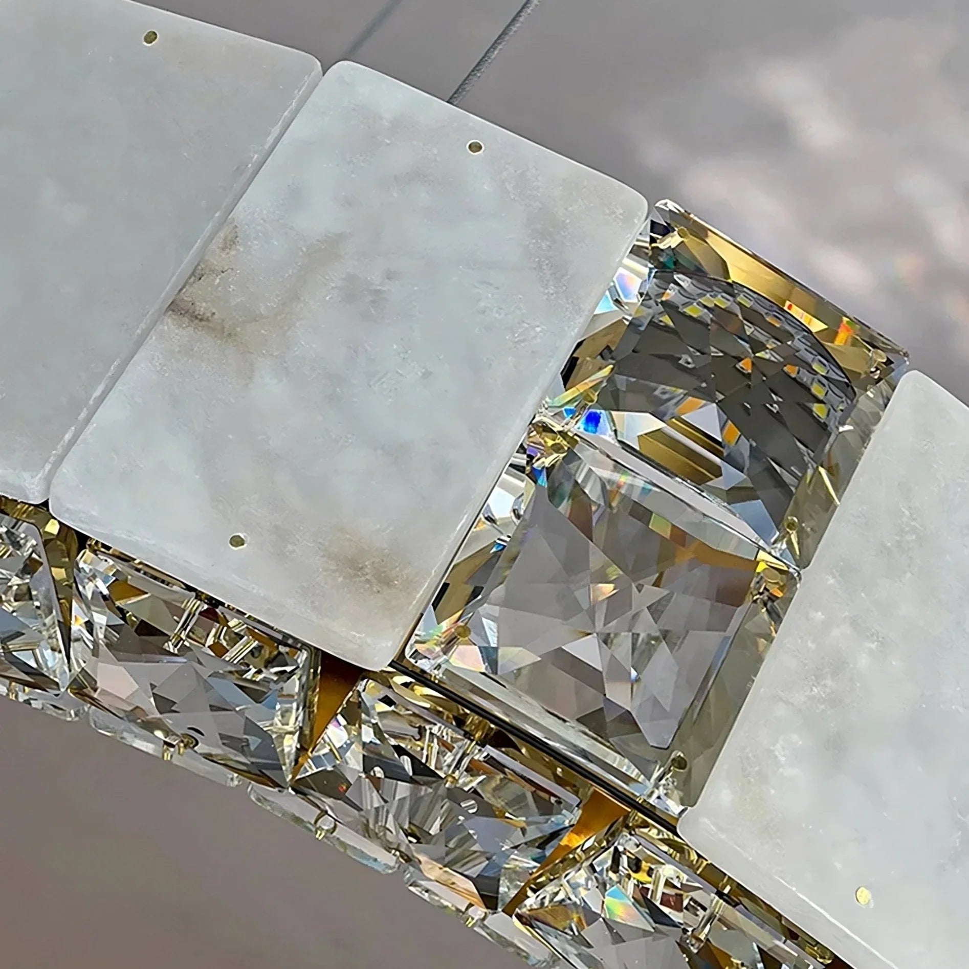 A close-up image shows a section of a luxurious Natural Marble & Crystal Modern Ceiling Light Fixture. The accessory from Morsale.com features large, square-cut, clear gemstones separated by rectangular, frosted metal or stone pieces with small holes. The design reflects light beautifully, reminiscent of a modern ceiling chandelier's sparkling effect.