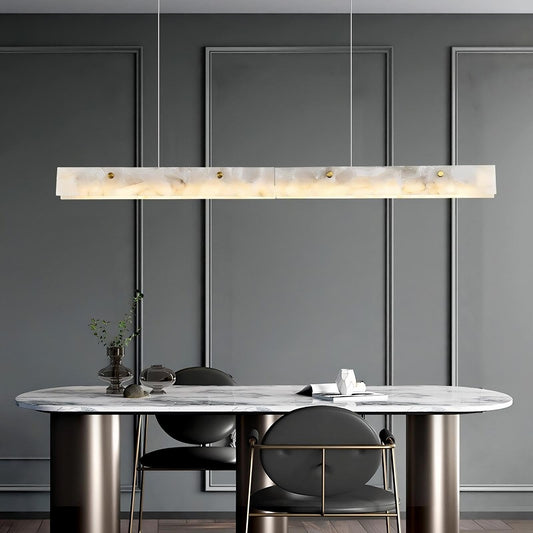 A modern dining room with grey paneled walls features a rectangular marble table with cylindrical legs. The 60" Natural Marble Dining Room Light Fixture by Morsale hangs elegantly above the table, providing chic and minimalist illumination. Two stylish grey chairs complement the setup, while a small vase with greenery and a few décor items enhance the luxurious design of the durable construction.
