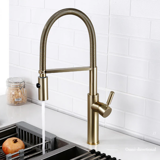 A modern Smesiteli Single Handle Pull Out Spout Kitchen Faucet with a high-arc, flexible neck and a matte gold finish is installed against a white tile backsplash. Water flows from the faucet into a sink that has a drain rack with a pomegranate on it. Nearby, a small jar of pasta enhances the elegant kitchen ambiance.