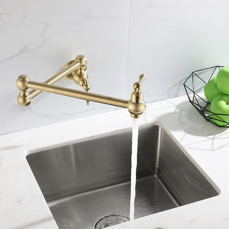 A Tiqui Kitchen Pot Filler Faucet with an adjustable arm is mounted on a white marble wall. The faucet is turned on, and water is flowing into a sink below. In the background, there's a fruit bowl containing green apples, adding a touch of freshness to the scene typical for elegant kitchen faucets or shower heads.