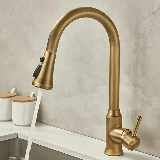 An Antique Brass Pull-Down Spout Kitchen Faucet by Rozin with a high arc and sleek, modern design pours water into a stainless-steel sink. The faucet handle is positioned to the right. In the background, reminiscent of elegant bathroom faucets, two white canisters with wooden lids are on a marble countertop.