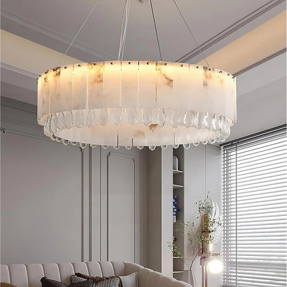 This modern living room, a luxury home decor highlight, features the Marble & Crystal Modern Chandelier by Morsale.com. The chandelier is large and circular with a frosted glass design. The room also boasts a light gray ceiling with crown molding, a tufted gray couch adorned with white pillows, and a floor lamp beside it. Blinds cover the window.