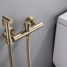 The Wasser™ Wall Mounted Toilet Sprayer Bidet Faucet by allfixture showcases a sleek, brass design. It includes a handheld sprayer on the left connected by a flexible hose, a central control knob, and an additional outlet on the right side, embodying the elegance of premium bathroom fixtures. The backdrop is light grey.