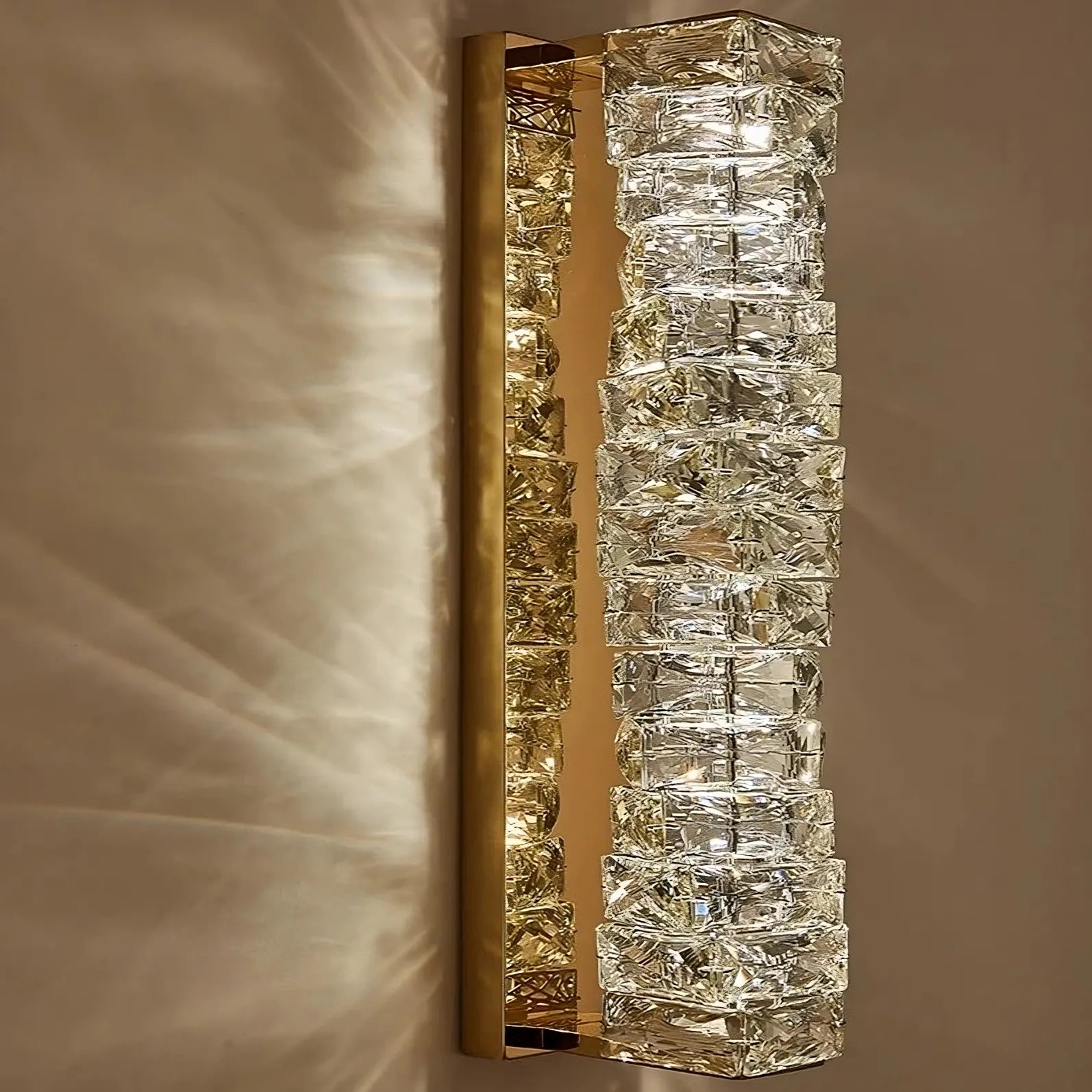 Introducing the Bacci Crystal Wall Sconces by Morsale.com, a rectangular wall fixture that boasts a brass frame and a gold metallic base adorned with an array of crystal-like glass cubes. This contemporary design illuminates your beige wall with shimmering effects and intricate light patterns.