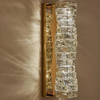 Introducing the Bacci Crystal Wall Sconces by Morsale.com, a rectangular wall fixture that boasts a brass frame and a gold metallic base adorned with an array of crystal-like glass cubes. This contemporary design illuminates your beige wall with shimmering effects and intricate light patterns.