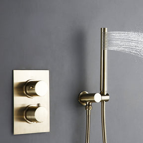 A modern bathroom featuring the Wasser™ Solid Brass Complete Shower System from Morsale.com, with a sleek rainfall showerhead mounted on a gray wall and a matching handheld shower faucet attached. Water cascades down as the shower is turned on. The room showcases a minimalist design with a white sink and a stone accent wall in the background.