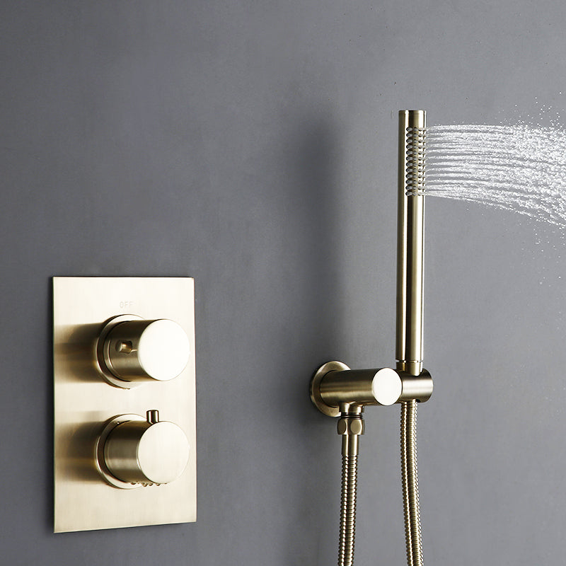 A modern bathroom featuring the Wasser™ Solid Brass Complete Shower System from Morsale.com, with a sleek rainfall showerhead mounted on a gray wall and a matching handheld shower faucet attached. Water cascades down as the shower is turned on. The room showcases a minimalist design with a white sink and a stone accent wall in the background.