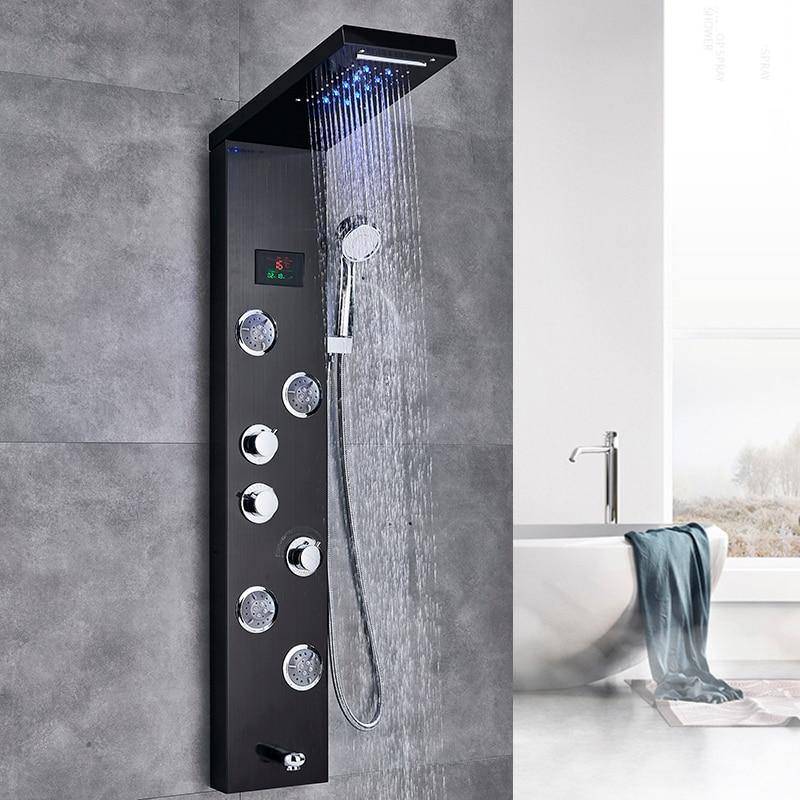 A Morsale.com 5-Stage LED Full Body Shower Panel With Massage Jets - Charcoal is mounted on a gray tiled wall. Water streams from the large overhead shower head, while multiple jets and a handheld showerhead enhance the modern design. In the background, there's a white bathtub with a towel draped over its edge.