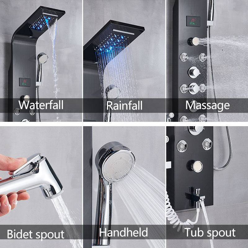 A stylish Morsale.com 6-Function Wall Shower Panel With Massage Jets in Charcoal is installed on a tiled wall. Water is flowing from the handheld shower faucet. To the right, a tall glass and metal plant stand holds several potted plants, with greenery visible outside.