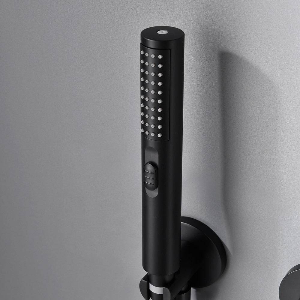 A brushed black rainfall showerhead from the Solid Brass Shower System by Morsale.com is mounted on a gray bathroom wall, with water streaming down. Below it are controls for the shower's temperature and water flow. To the right is an attached handheld showerhead with a flexible hose. Nearby, matching bathroom sink faucets complete the sleek design.