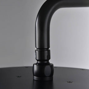 A Complete Shower System With Handheld Sprayer in Matte Black from Morsale.com is mounted on a grey wall, releasing a stream of water. Below the showerhead are two black wall-mounted control knobs and a handheld shower attachment.