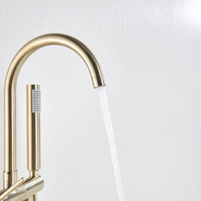 A modern bathroom featuring a sleek, golden Wasser™ Floor Mounted Bathtub Filler Shower System from Morsale.com with water flowing into a white bathtub. The background showcases a gray textured wall and a partially visible white curtain on the left side. A beige towel hangs over the edge of the tub, complementing the elegant bathroom faucets.