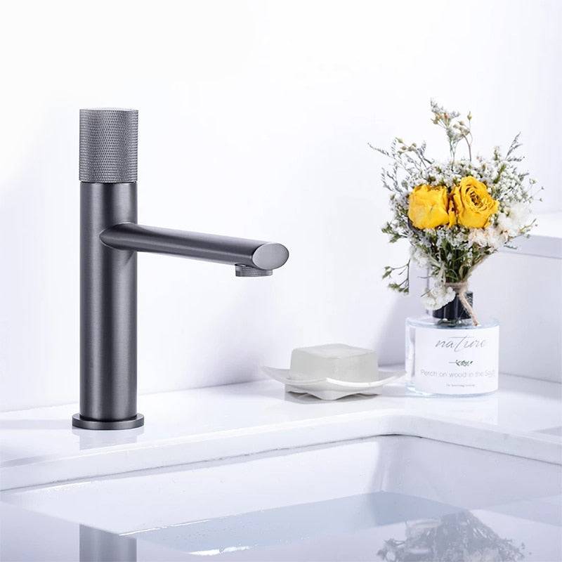 The Wasser™ Brass Bathroom Sink Faucet by Morsale.com, with its sleek, modern black design, is installed over a white basin. To the right, a clear vase holds a bouquet of yellow roses and greenery. A white soap dish with soap sits near the vase, enhancing the clean and minimalistic aesthetic.