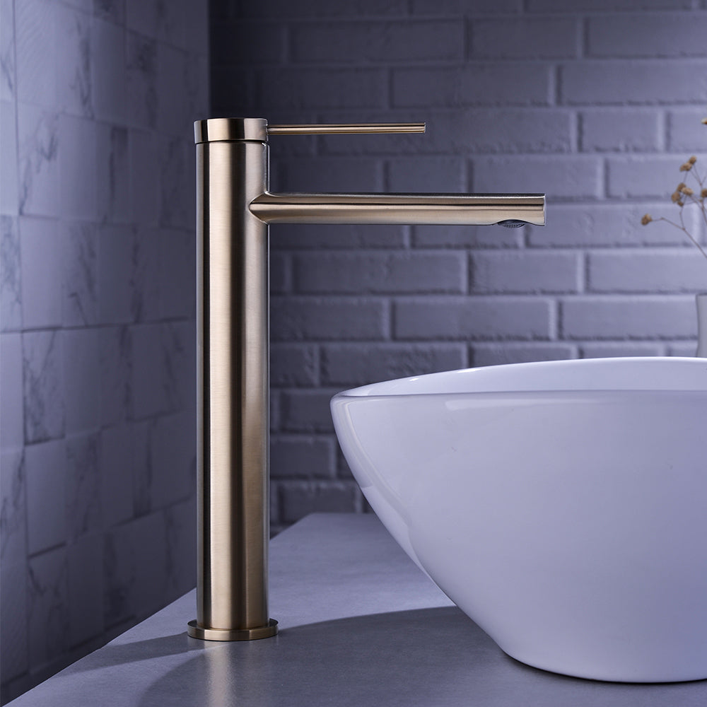 A modern bathroom sink with a cylindrical Wasser™ Solid Brass Single Handle Bathroom Faucet in brushed brass from Morsale.com. The sink is a white, oval vessel sitting on a grey countertop. The background features white subway tile and a grey marble wall, complete with a matching brushed brass shower head, giving the bathroom a sleek and stylish appearance.