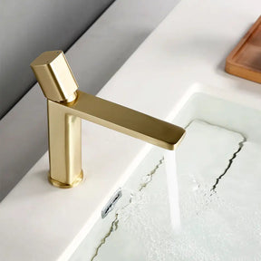 A sleek, modern Wasser™ Solid Brass Bathroom Sink Faucet from Morsale.com pours water into a rectangular white sink. The water flows smoothly, creating ripples in the filled basin. The background includes a gray wall and a corner of a wooden tray on the countertop.