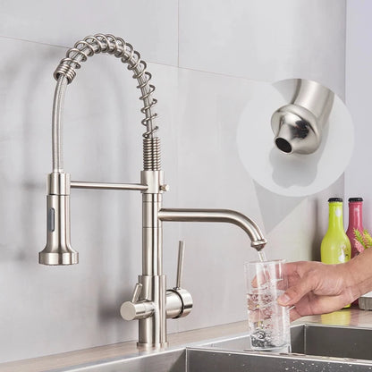 A MyQualife Double Handle Pull-Out Spout Kitchen Faucet with a high, curved design and flexible spring installation is installed over a stainless steel sink. The kitchen faucet features a versatile pull-out spray head and dual lever handles for water control. In the background, colorful bottles adorn the counter.