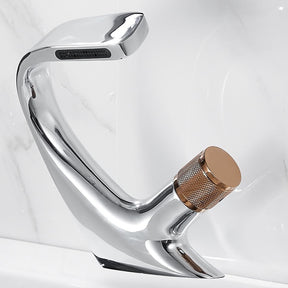 Close-up of an AllFixture Solid Brass Bathroom Basin Faucet with a modern, sleek black finish and angular design, installed on a white sink. Water is flowing from the faucet. In the background, a blurred image shows two toothbrushes in a holder on the countertop. The sink backdrop is a light-colored marble surface.