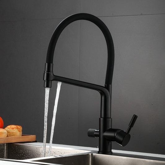 A Matte Black Kitchen Faucet With Filtered Water Tap by Rozin, featuring a high-arc gooseneck design, is installed over a stainless steel sink. Water is flowing from its spout. In the background, bread rolls and a tomato rest on a wooden cutting board, contrasting beautifully against the matte gray wall.