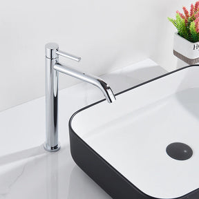 A Rozin Single Handle Deck Mounted Bathroom Sink Faucet in chrome dispenses water into a rectangular black-and-white basin. In the background, a small plant in a white pot adds a touch of greenery to the sleek, minimalist bathroom setting, perfectly complementing the nearby shower head.