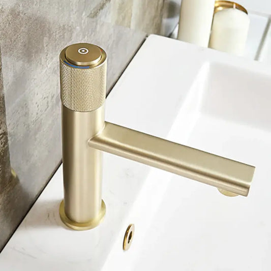 A modern, cylindrical Knob Switch Solid Brass Bathroom Sink Faucet in brushed gold by Wanfan installed on a white countertop. The faucet features a single lever and minimalist design, accented with textured detailing on the handle for improved grip. In the background, part of the rectangular sink and additional bathroom faucets can be seen.