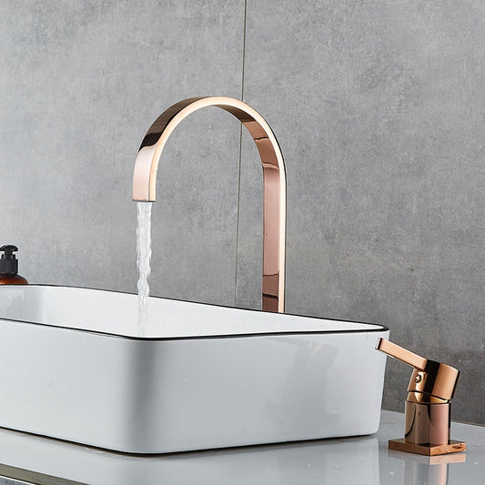 A modern bathroom sink with a rectangular white basin featuring black trim is shown. Water flows from AllFixture's sleek, U-shaped, rose gold Single Handle Deck Mounted Bathroom Faucet. Additionally, a matching rose gold lever handle and soap dispenser are visible on the gray countertop—perfect for coordinating with any stylish bathroom sink faucet or shower head.