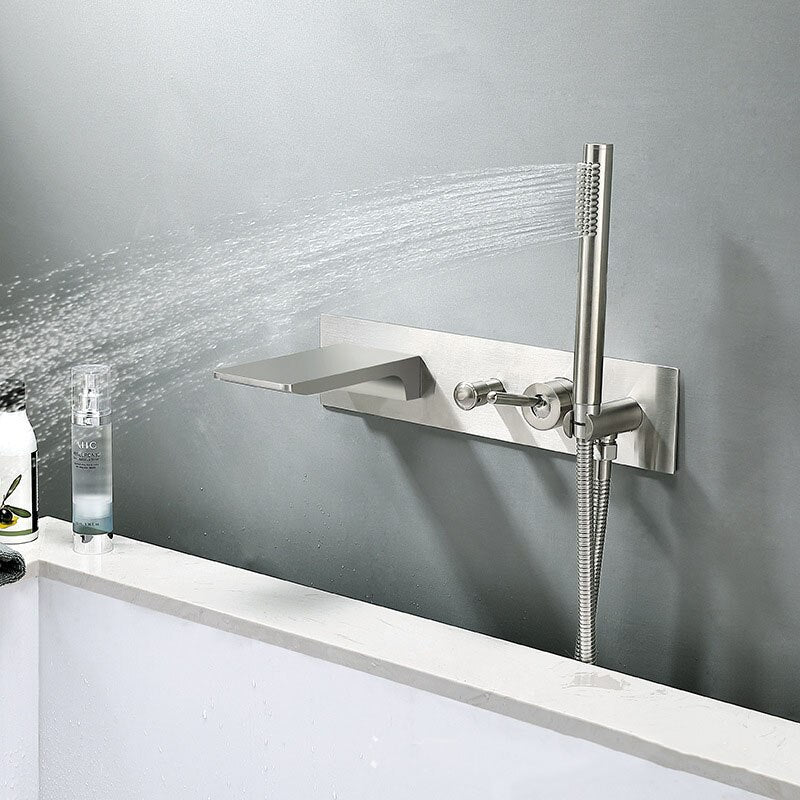 The Sekova Wall Mounted Bathtub Faucet With Handheld Shower Sprayer is depicted. It features a modern design with a sleek, rectangular spout that allows water to flow smoothly. Adjacent to the spout, on the same panel, is a handheld showerhead equipped with a hose. Both the fixture and the surrounding wall boast a brushed stainless steel finish.