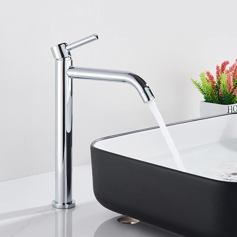 A Rozin Single Handle Deck Mounted Bathroom Sink Faucet in chrome dispenses water into a rectangular black-and-white basin. In the background, a small plant in a white pot adds a touch of greenery to the sleek, minimalist bathroom setting, perfectly complementing the nearby shower head.