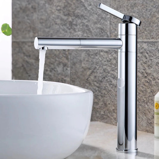 A modern Wanfan Wasser™ Single Handle Sink Faucet with a sleek, chrome finish is dispensing water into a white, ceramic basin sink. The background showcases a textured grey stone wall, and a bottle of soap is placed to the right of the sink on the countertop.