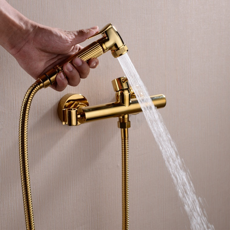 A hand holding the Wasser™ Solid Brass Handheld Toilet Sprayer by allfixture, attached to a matching wall-mounted fixture, much like elegant bathroom faucets. Water is spraying from the sprayer, and the scene is set against a light-colored backdrop.