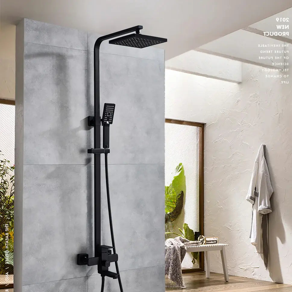 A modern bathroom featuring the AllFixture Solid Brass Rainfall Bath Shower System with a gold-finished square rain shower head and an adjustable handheld showerhead, all mounted on a gray tiled wall. A towel hangs on the adjacent white textured wall, and a glass door opens to a sunlit room, accentuating the elegant design of the shower faucet.