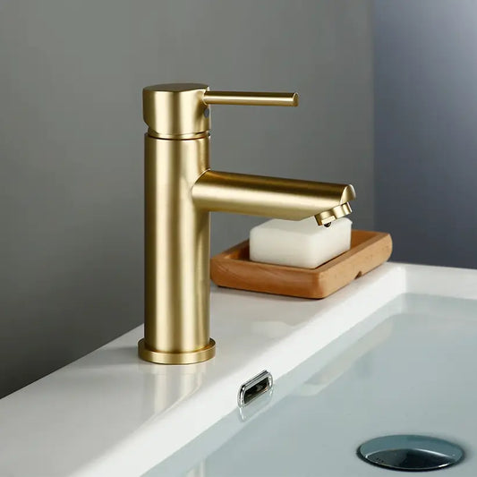 The Wasser™ Brushed Gold Solid Brass Bathroom Faucet by allfixture, featuring a sleek, modern design with a single lever handle, is positioned over a white sink with water flowing from the spout. In the background, a soap dish with a bar of soap adorns the countertop. This elegant faucet seamlessly complements other bathroom faucets and fixtures in your home.