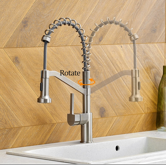 A modern kitchen faucet from allfixture, the Wanfan™ Pull Out Single Handle Swivel Kitchen Faucet, is pictured with a brushed stainless steel finish. It features a flexible coil spring spout and a pull-down spray head. Shown in two positions to illustrate its rotation capability, highlighted by an orange arrow, the faucet's quality is comparable to that of high-end bathroom fixtures.