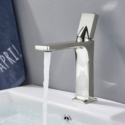 An AllFixture Deck Mounted Brass Single Handle Brass Basin Faucet in modern black matte is attached to a white counter. It is pouring water into a white, round basin with blue stripes near the rim. The counter is decorated with a vase of colorful dried flowers in the background.