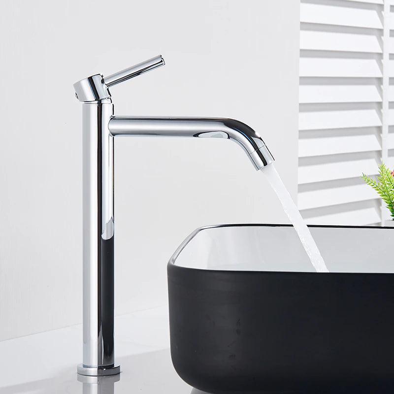 A Rozin Single Handle Deck Mounted Bathroom Sink Faucet in chrome dispenses water into a rectangular black-and-white basin. In the background, a small plant in a white pot adds a touch of greenery to the sleek, minimalist bathroom setting, perfectly complementing the nearby shower head.