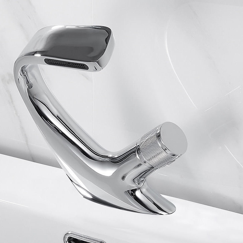 Close-up of an AllFixture Solid Brass Bathroom Basin Faucet with a modern, sleek black finish and angular design, installed on a white sink. Water is flowing from the faucet. In the background, a blurred image shows two toothbrushes in a holder on the countertop. The sink backdrop is a light-colored marble surface.